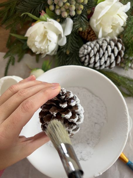 This DIY project will add a touch of winter magic to your home! Using flocking powder, turn plain pinecones into frosted, snowy beauties that are perfect for winter decorating. Follow our step-by-step tutorial and have a basket full of frosted pinecones in no time. These DIY pinecones will bring a touch of winter wonder to any room. Grab your flocking powder and pinecones, and let's get crafting! White Pinecones Diy, Diy Pinecone Ornaments Xmas, Christmas Crafts Using Pine Cones, Diy Frosted Pinecones, Glitter Pine Cones Diy, Snow Covered Pinecones, How To Frost Pinecones, Prepping Pinecones For Crafts, Spray Painting Pine Cones Diy