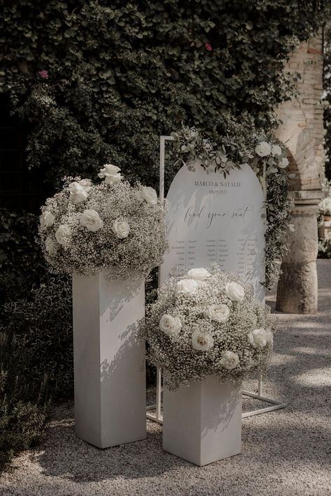 White roses and white gypsophila with white wedding table plan signage Wedding Decorations White Roses, Wedding With Peonies, White Black Sage Wedding, Wedding Table Decorations White Flowers, White Wedding Flowers Table Decor, White Rose Isle Wedding, White Roses And Gypsophila Wedding, Babies Breath And White Roses Wedding, White Wedding Flowers Decor