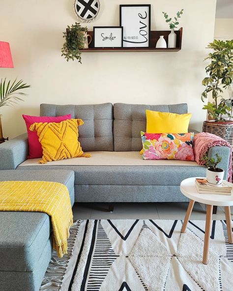 The grey sofa acts as a neutral anchor for the contemporary living room design, allowing the vibrant colors to shine. The bright yellow and pink shades of the cushions create a playful contrast against the grey backdrop. In the heart of the room, a round coffee table sits atop a beautiful, patterned carpet. Above the sofa, a stylish shelf is mounted on the wall, showcasing an assortment of ceramic vases, indoor plants and frames. Cr: mi_colourfulworld Living Room Decor Grey Sofa, Colorful Living Room Bright, Quirky Living Room, Living Room Inspiration Grey, Sofa Set Living Room, 1 Seater Sofa, Fabric Sofa Design, Grey Sofa Living Room, Vibrant Living Room