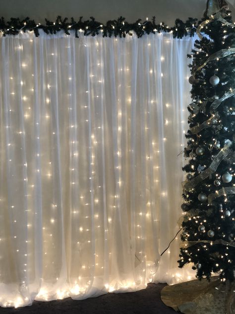 Christmas Backdrop (Pipe and Drape with string lights and greenery. Christmas Photo Corner Ideas, Christmas Party Room Decorations, Christmas Drapes Ideas, Winter Theme Backdrop, Christmas Pictures Backdrop, Diy Santa Photo Backdrop, Winter Party Backdrop, Simple Christmas Backdrops For Photos, Christmas Wedding Photo Backdrop