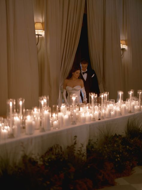 This wedding reception head table was covered in pillar candles and lined with organic florals. The bride and groom were seated with their nearest and dearest bridal party members. The draped ballroom made for the most stunning moody wedding. Candle Reception Table Decor, Candle Bridal Table, Moody Wedding Reception Table, Wedding With Candles Everywhere, Moody Night Wedding, Candles And Lights Wedding, Moody Wedding Draping, Bridal Table Candles, Romantic Candle Light Wedding