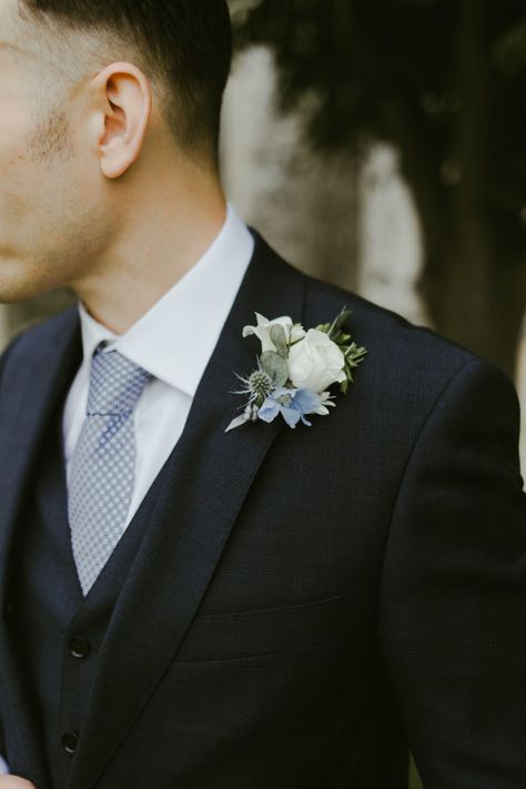 White flower buttonhole with blue suit and tie Blue And White Buttonhole, Blue Buttonholes Grooms, White And Blue Buttonhole, Black Suit Dusty Blue Tie, Wedding Flowers Men, Blue Boutineer, Black Suit Blue Tie, Blue And White Boutonniere, Powder Blue Bridesmaid