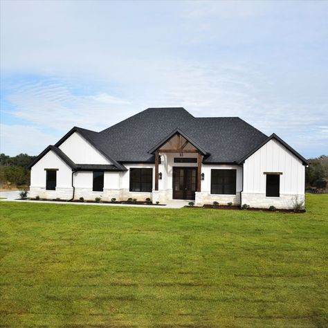 White farmhouse exterior with white vertical siding, black windows, black roof, white rock exterior, cedar trellis and cedar details White Ranch Black Windows Exterior, White Siding Black Roof Farmhouse, White House Vertical Siding, White Brick House Farmhouse, White Farmhouse Black Trim Exterior, White Brick Black Roof House, White Black House Exterior Modern, White Barndominium With Black Trim, Black And White House Paint Exterior