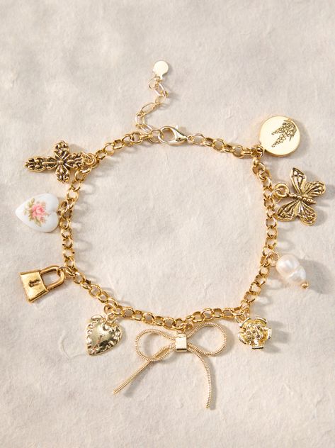 This bracelet features a bow charm with butterfly, cross, pearl, heart, lock, flower, and lilac accents, adding a touch of elegance to any outfit. Jewelry Gold Dainty, Jewelry Charm Bracelets, Altered State Jewelry, Gold Charm Jewelry, Coquette Charm Bracelet, Homemade Charm Bracelets, Pretty Jewellery Bracelets, Cute Jewelry Gold, Basic Jewelry Essentials