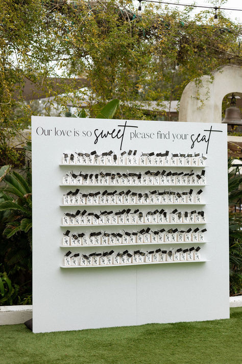 This San Diego wedding took place at Tivoli the Italian inspired wedding estate. A creative seating chart was designed, featuring a shelf adorned with cookies, each bearing the name of a guest. These yummy treats were more than just a place card; they also featured the couple’s personal monogram. Photographer: JC Jones | Seating Chart Wall: Rent Boho Babes Seating Chart Cookies, Creative Seating Cards Wedding, Wedding Seating Chart Favors, Wedding Favor Seating Chart Ideas, Creative Seating Chart Wedding Party Favors, Custom Wedding Seating Chart, Custom Seating Chart Wedding, Cookie Seating Chart Wedding, Matchbook Seating Chart