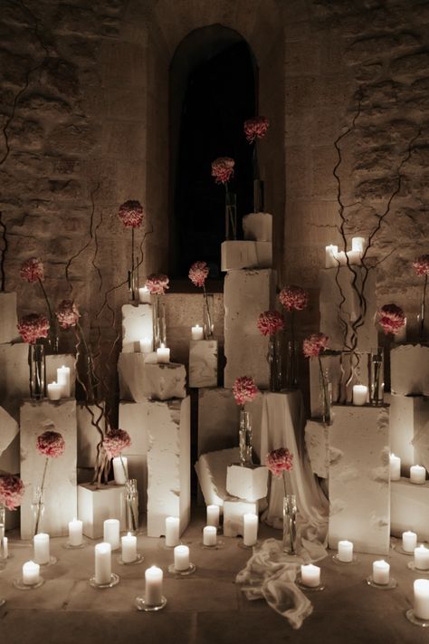 Elodie Villemus used 450 candles to create the perfect contrast against the ancient stones of the chapel. This also helped create the perfect ceremony space featuring white votives surrounding concrete blocks adorned with single stem vases. Pink was the perfect floral color choice to help create a pop of soft color against the stones. Candle Wedding Ceremony Altars, Negative Space Wedding, Candle Installation, Ceremony Space Decor, Concrete Wedding, Rose Ceremony, Stone Structures, Ceremony Candles, Intimate Ceremony