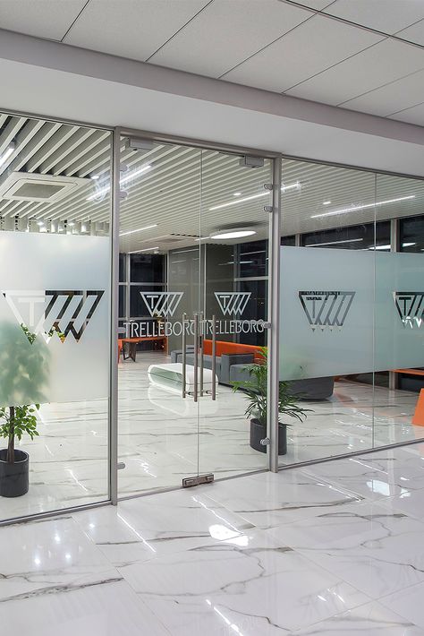 Glass Frosting can be a sure way of highlighting your branding at the workspace. When ZYETA designed the new Trelleborg's office space, the brand's logo was beautifully decorated on the glass doors, depicting brand marketing. #glassfrostingdesign #officeinteriors #workspacedesign #glassdoordecor Frosted Logo On Glass Door, Frosted Glass Office Doors, Marketing Office Interior Design, Glass Film Design Office Patterns, Glass Paper Design, Glass Sticker Design Office, Office Glass Design, Office Glass Door Design, Office Door Design