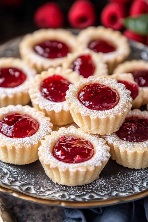 Assorted mini raspberry almond tarts displayed on a silver tray, each tart with a golden crust, filled with rich raspberry jam, and topped with a light dusting of powdered sugar. Pastry Baking Recipes, Round Petit Fours, Easy Mini Tart Recipes, Mini Raspberry Almond Tarts, Raspberry Christmas Cookies, Christmas Slice Recipes, Rasberry Tart Recipes, Christmas Mini Tarts, Christmas Party Food Desserts