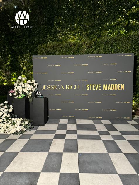 Guests were welcomed by a striking black and gold step and repeat, showcasing Jessica's favorite shoes on sleek black podiums, all accented with elegant white floral installations.  #wotp #thewotp #wifeoftheparty #partyplanner #eventplanning #thewotp #thewifeoftheparty #event #eventplanner #events #losangelesevents #wecelebratepeople #loriannserna #stevemadden #stevemaddenxjessicarich #shoes #collaboration #thependrywesthollywood Luxury Corporate Event Decor, Corporate Backdrop Design Events, Corporate Event Photo Booth, Company Event Decoration, Event Set Up Ideas, Step And Repeat Ideas, Conference Decorations Events, Event Photo Wall, Black And White Event Decor