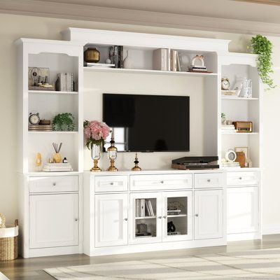 This wall unit features a 57-inch console, two pier units, and an overhead bridge providing ample storage options. This media unit features sliver finished knobs, glass doors with wood framing, open storage, and storage drawers. The console will accommodate most 55" TV. The elegant and minimalist white finish is suitable for any home decoration environment. | Wildon Home® Inverleigh Entertainment Center for TVs up to 55" Wood in Brown / White | Wayfair Built In Tv Cabinet, White Tv Cabinet, Built In Wall Units, Entertainment Wall Units, Built In Entertainment Center, Built In Shelves Living Room, Living Room Wall Units, Living Room Built Ins, Living Room Entertainment Center