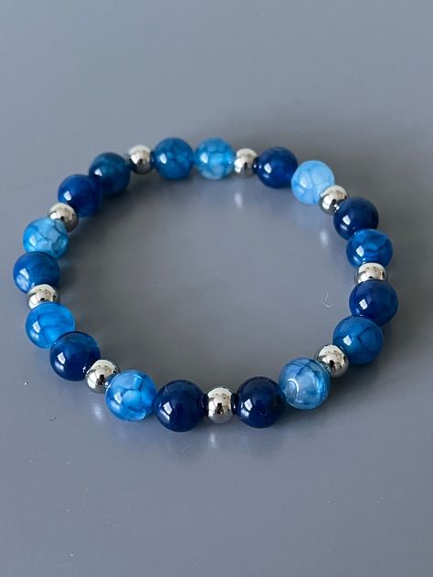 Beautiful blue dyed crackle agate gemstones bracelet will standout! Silver beads are stainless steel to prevent tarnishing. The beads are 8mm and silver beads are 6mm. Bracelet measures 7 inches. Beads are strung on durable 8mm elastic.  These are natural stones, so appearance of  beads on your bracelet may be different than pictured.  Please take care when putting in your bracelet to avoid excessive stretching. Roll bracelet onto wrist.  We hope you enjoy this one! Blue Bracelets Diy, Blue Gem Bracelet, Natural Stone Beads, Natural Bead Bracelets, Blue Beaded Bracelets With Gemstone Beads For Gift, Blue Crystal Beaded Bracelet, Blue Bracelet Beads, Blue Beaded Bracelets With Natural Stones, Adjustable Blue Gemstone Bead Bracelets