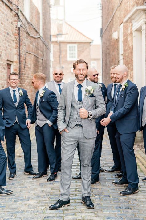 Groom in a light grey check wedding suit with his groomsmen in navy three-piece suits standing behind him | Caro Patrick Photography Grey Suit Navy Tie Wedding, Grey Groom Suit With Bride, Grey Suits For Men Color Combos, Grey Suit With Navy Tie, Grey And Blue Suit, Grey Suit Blue Tie, Navy Grey Suit, Groomsmen Attire Grey, Grey Tuxedo Wedding