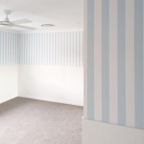 Selecting the perfect shade of blue striped wallpaper & complementing it with pristine white VJ paneling sets the stage for a delightful space tailored for a young man. The shade of blue sets the tone for the entire room & this lighter shade evokes a sense of serenity & relaxed ambiance, perfect for an active young man's bedroom to encourage rest & sleep. Striped wallpaper adds visual interest & dimension to the walls, creating a dynamic backdrop for the room's decor. Vertical stripes add ... Blue And White Striped Wall, Striped Nursery Walls, Striped Wallpaper Nursery, Striped Walls Bedroom, Blue Striped Walls, Stripe Wallpaper Bedroom, Young Mans Bedroom, Blue Stripe Wallpaper, Striped Bedroom