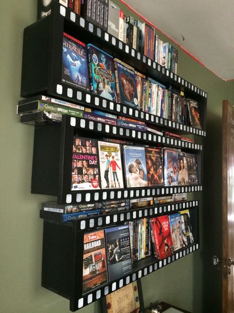 Home made wall-mounted DVD storage.  Painted black.  The 1x2 face trim is stamped with white squares to roughly replicate the little holes on a filmstrip.  Holds about 370-380 standard DVDs Movie Display Ideas, Dvd Storage Aesthetic, Movie Storage Ideas, Vhs Storage Ideas, Dvd Display Ideas, Movie Collection Display, Camera Display Ideas, Bluray Storage, Diy Dvd Shelves