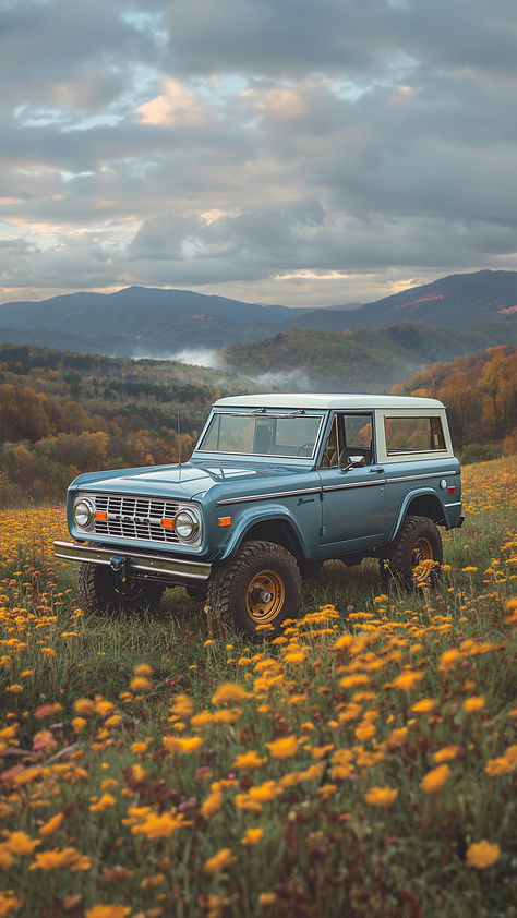 A vintage blue Ford Bronco stands in a vibrant field of yellow wildflowers, with the smoky blue hills of the Tennessee mountains rising in the background under a dramatic sky. Blue Ford Bronco Aesthetic, Bronco Ford Aesthetic, 2 Door Bronco, Ford Bronco Aesthetic, Bronco Aesthetic, Blue Ford Bronco, Country Cars, Tennessee Landscape, Bronco Jeep