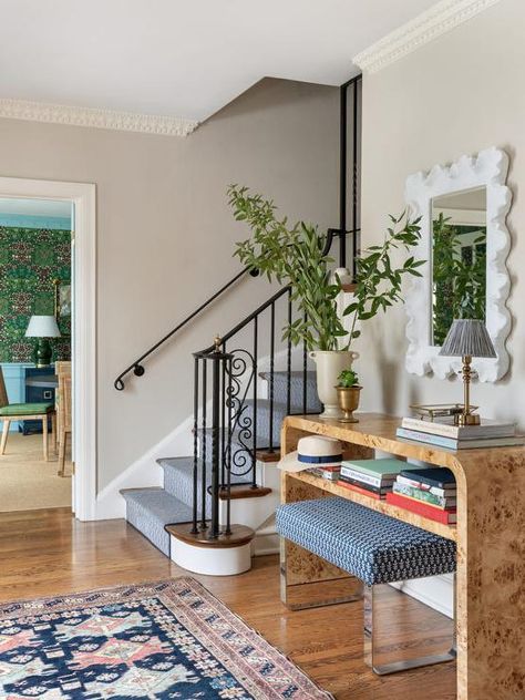 A red and blue rug sits in front of a blue stool placed beneath a burl wood waterfall console table, styled with stacked books and located under a white scalloped mirror. Burlwood Entry Table, Burlwood Console Table, White Scalloped Mirror, Dresser Styling Ideas, Sicilian Interior, Create An Entryway, Wood Entry Table, Sleek Console, Dresser Styling