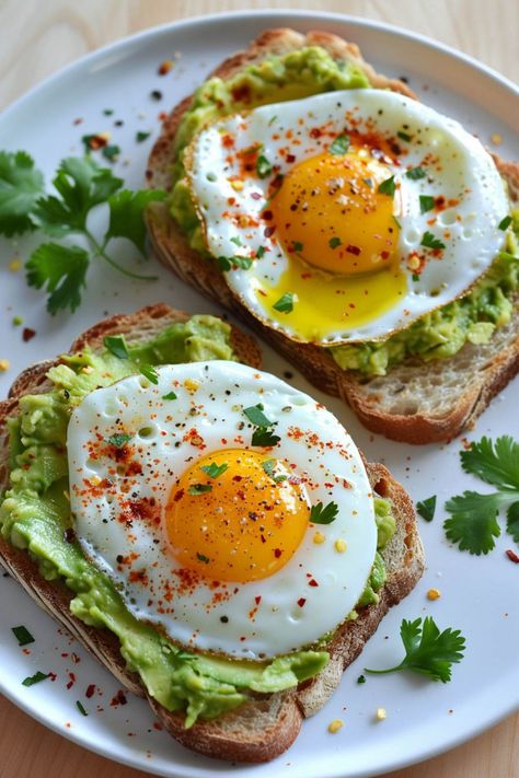 Two slices of avocado toast topped with fried eggs and a sprinkle of red seasoning, garnished with fresh cilantro leaves on a white plate. Healthy Vegetarian Recipes Breakfast, Breakfast Ideas Avocado Toast, Toppings For Toast, Easy Breakfast Toast, Healthy Recipes Breakfast Easy Mornings, Romanticize Your Morning, Easy Breakfast Toast Ideas, Healthy Breakfast Avocado Toast, Avacodo Toast Recipes Breakfast Eggs