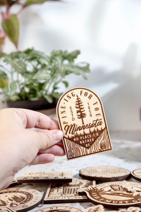 Pine-ing For You Minnesota Engraved Wood Magnet Our Wood Magnets are designed and crafted in-house from quality 1/4 in. engraved plywood. Magnets make great souvenirs from favorite travels, keep track of notes and those pesky to-do lists, or add a little humor to your home or office. +Magnet is about 2.5 in by 3.5 in in size +Quality 1 in. Black Ceramic button Magnet and Attached with a 2-Part Epoxy for strength. +Wood is given a matte finish to seal laser engraving. Please note the color can va Custom Laser Engraving, Cricut Wood Engraving, Travel Souvenirs Ideas, Laser Magnets, Laser Engraving Ideas To Sell, Laser Printer Projects, Wood Laser Engraving Ideas, Laser Engraving Ideas Gifts, Laser Engraving Ideas