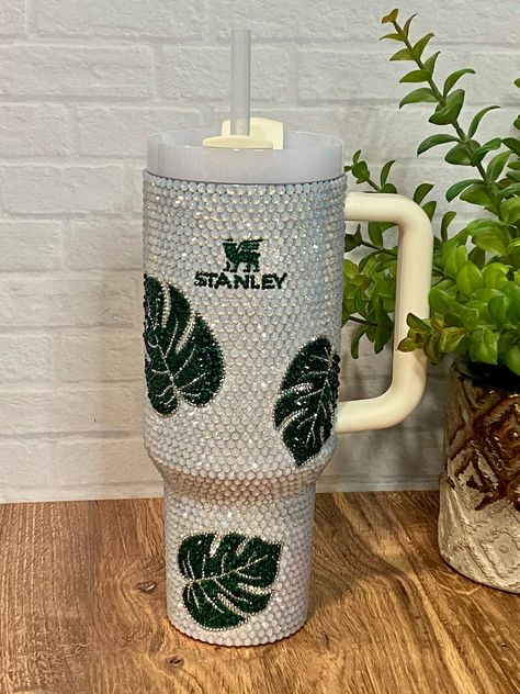 Everyone needs a little BLING on their Stanley! This authentic 40oz cream Stanley stainless steel, double-wall tumbler is fully blinged with AB Opal glass Rhinestones and Emerald Green glass rhinestones for the logo. Silver rhinestones outline with leaves.  View my video to see the AMAZING sparkle this Monstera Leaf tumbler gives off! I place each rhinestone by hand, one by one.  40 oz tumblers typically take 14-24 hours, depending on the design. Lid & Straw are included.  Stanley Tumblers are c Rhinestone Stanley Tumbler, Stanley Cups Decorated, Rhinestone Cup Ideas, Rhinestone Stanley Cup, Cup Decorating, Rhinestone Cups, Cute Coffee Cups, Double Wall Tumblers, Rhinestone Projects