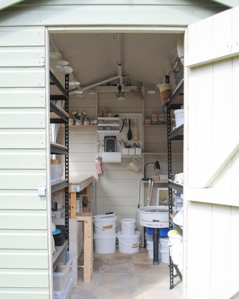 Pottery studio/shed, photographed from the door. The exterior of the shed is light green, whilst the interior is cream. In shot, you can see shelving units, a workbench, a pottery wheel and tools lining the walls. Small Ceramic Studio Ideas, Kiln Shed Outdoor, She Shed Pottery Studio, Pottery Studio Setup Ideas, Small Home Pottery Studio Setup, Small Home Pottery Studio, Mini Pottery Studio, Outdoor Pottery Studio, Pottery Organization