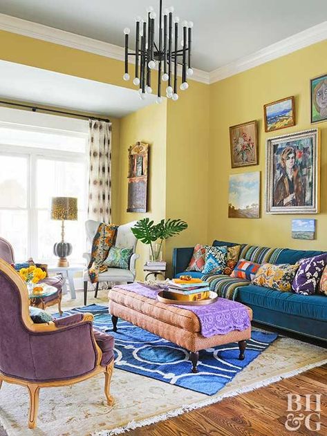 Yellow is one of many colors featured in this eclectic living room. The yellow walls host a gallery of colorful art, and a pacific blue sofa holds plenty of patterned pillows. Layered rugs soften the space, while yellow living room accessories, like fresh flowers, a lampshade, and throw pillows, incorporate the sunny color scheme throughout. Yellow Living Room Accessories, Yellow Walls Living Room, Yellow Decor Living Room, Yellow Wall Decor, Furnitur Ruang Keluarga, Yellow Room, Yellow Living Room, Living Room Color Schemes, Yellow Decor