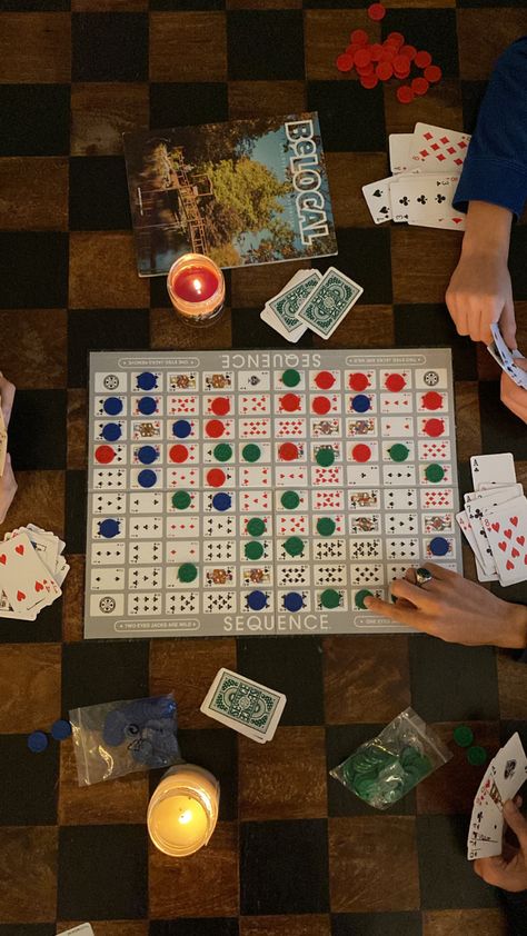 top-down overhead photo of sequence (the board game) splayed across a black and brown wooden coffee table as three people are playing the game, two candles are lit on the table Checkers Game Aesthetic, Family Board Games Aesthetic, 30th Birthday Cabin Weekend, Cabin Weekend Activities, Cozy Cabin Vibes, Board Game Coffee Table, Cabin Party Aesthetic, Family Game Night Aesthetic, Summer Cabin Aesthetic