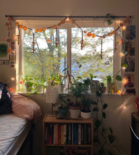 Picture of bed next to window with flower and orange garland hanging from curtain rod with plants on the windowsill. College Dorm Room Ideas Cottagecore, Cute College Dorm Decor, Earthy Dorm Room Ideas Vintage, Dorm Aesthetic Retro Vintage, Dorm Apartment Decor College, Dorm Window Decor, Cosy Dorm Room, Overhead Bed Decor, Cozy Room Fall