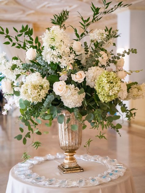 Large centerpiece made with pops of whimsical greenery such Eucalyptus and Italian Ruscus. The flower colors went with the neutral hues used in the Bride's bouquets with soft touches of blush. Big Floral Arrangements Wedding, White Wedding Arrangements Centerpieces, Wedding Flower Arrangements Centerpiece Head Tables, Tall Vase Bouquet, Neutral Flower Arrangements Centerpieces, Tall Flower Arrangements For Table, Green And White Flower Arrangements Tall Centerpiece, Flower Bouquet For Table, Winter White Flower Arrangements