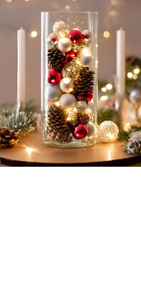 A tall, elegant glass vase filled with small, shiny Christmas ornaments, natural pinecones, and softly glowing fairy lights. The combination creates a warm and festive centerpiece for a holiday table Ornament Candle Centerpiece, Table Decorations Christmas Party, Christmas Decoration For Home, Christmas Deco Table Ideas, Ornaments Table Decor, Cute Christmas Decorations For House, Christmas Ornaments In A Glass Vase, Christmas Decor Ideas Office Party, Ornament Table Decor