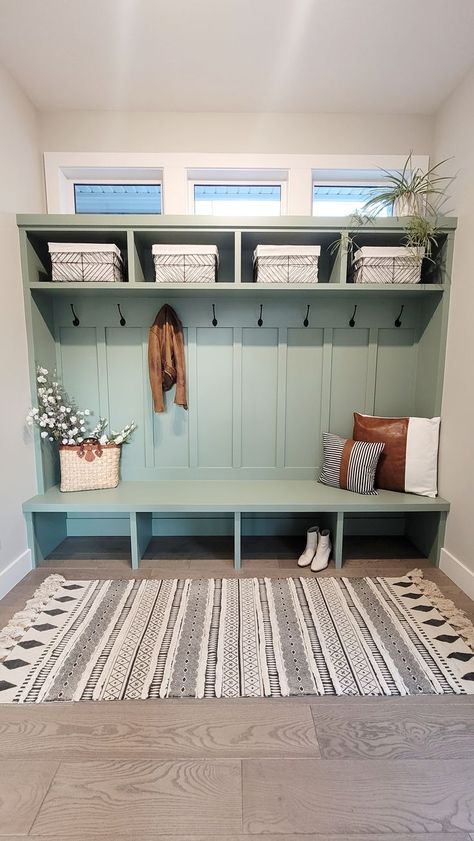 Mudroom cubbies and storage in a light greenish blue color with white and black wire storage baskets, brown leather and white cotton accent pillows, rattan bag with flowers, brown leather jacket and white boots. Hampton Style Home, Refresh Home, Functional Mudroom, Mudroom Remodel, Mudroom Makeover, White Tile Backsplash, Mudroom Decor, Mud Rooms, Mud Room Storage