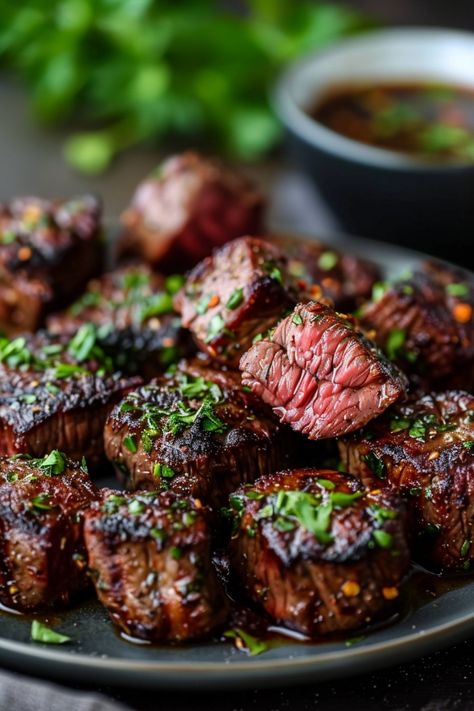 Grilled beef steak bites garnished with herbs on a plate, with a bowl of dipping sauce in the background. Air Fryer Steak Kebab Recipes, Air Fry Steak Bites Recipes, Air Fryer Teriyaki Steak Bites, Ribeye Steak Bites In Air Fryer, Healthy Air Fryer Steak Bites, What To Make With Ribeye Steaks, Steak Bits In Air Fryer, Air Fry Garlic Butter Steak Bites, Airfry Steak Bites Recipe