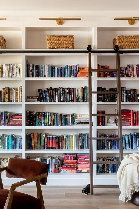 A ladder on rails complements floor-to-ceiling built in bookcases lit by brass picture lights. Summer Room Ideas, Luxury Bookcase, Vibey Apartment, Farmhouse Bookshelf, Styling A Bookcase, Floor To Ceiling Bookshelves, Industrial Farmhouse Decor, Summer Room, Mini Gym