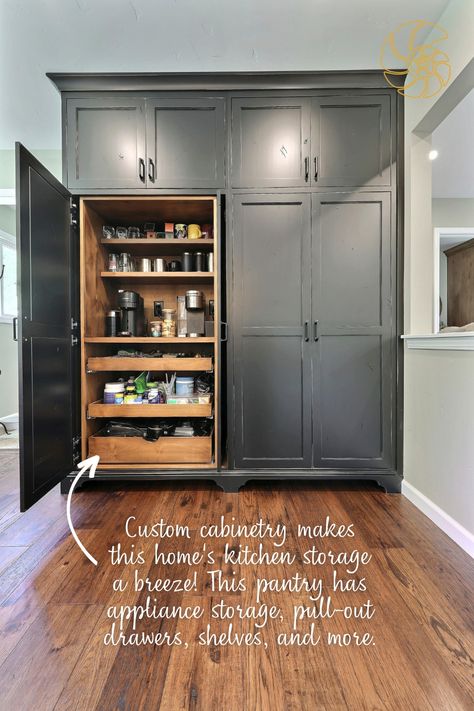 A floor-to-ceiling custom pantry with black cabinets and natural wood interior. The large pantry has French hideaway doors, which are seen in action as half of the pantry is open in the image. Inside the cabinet are two coffee machines, pull-out drawers, and plenty of shelving. The image has text that reads, "Custom cabinetry makes this home's kitchen storage a breeze! This pantry has appliance storage, pull-out drawers, shelves, and more." with an arrow pointing to the interior of the pantry. Pantry Wall Ideas Built Ins, Standalone Pantry, Built In Pantry Cabinet Wall, Barndo House, Lakehouse Kitchen, Whole House Remodel, Kitchen 2024, Built In Pantry, Custom Pantry