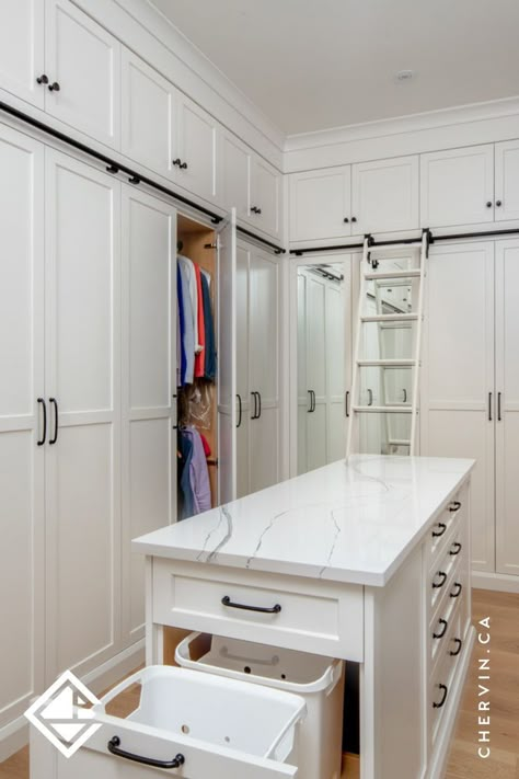 A white walk-in closet with a rolling ladder and Walk In Closet Seating Ideas, Closet With Middle Island, Master Closet Center Island, Closet Pull Out, Closet With Ladder Small Spaces, Walk In Closet Design With Island, Small Closet With Island, Walk In Closet Ideas Farmhouse, Master Closet With Island And Vanity