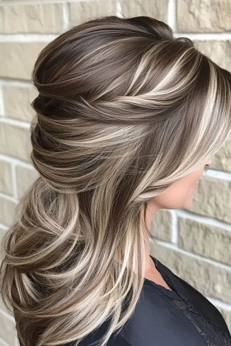 Woman with long, layered hairstyle featuring blonde highlights against a brick wall background. Hair Color Ideas For Brunettes Platinum, Dark Brown Light Brown And Blonde Hair, Best Hair Color To Camouflage Gray, Blonde Over Dark Hair, Mocha And Blonde Highlights, Hair Color Ideas For Brunettes Going Lighter, Winter Highlights And Lowlights, Vanilla Highlights Brown Hair, Mocha Latte Hair Color