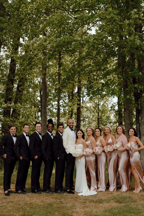 Wedding party in black groomsmen suits and pink satin bridesmaid dresses. Black Tux And Champagne Wedding, Rose Gold Bridal Party Groomsmen, 6 Bridesmaids And Groomsmen, Blush Pink Bridesmaid Dresses With Groomsmen, Desert Rose Bridesmaid Dresses And Groomsmen, Champagne Pink Bridal Party, Groomsmen Attire Blush Color Schemes, Bride Groom Bridesmaids Groomsmen, Wedding Ceremony Bridesmaids Groomsmen