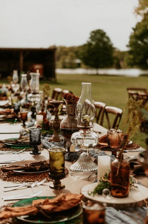 This moody cottage core wedding had the perfect al fresco tablescape! We love the vintage glassware and foraged florals. Check out more outdoor dining ideas on our blog. Boho Thrifted Wedding, Cottage Core Forest Wedding, October Moody Wedding, Thrifted Wedding Bridesmaid Dresses, Fall Wedding Farmhouse, Bohemian Table Setting Wedding, Vintage Fall Wedding Decorations, Earthy Wedding Inspiration, Antique Rustic Wedding