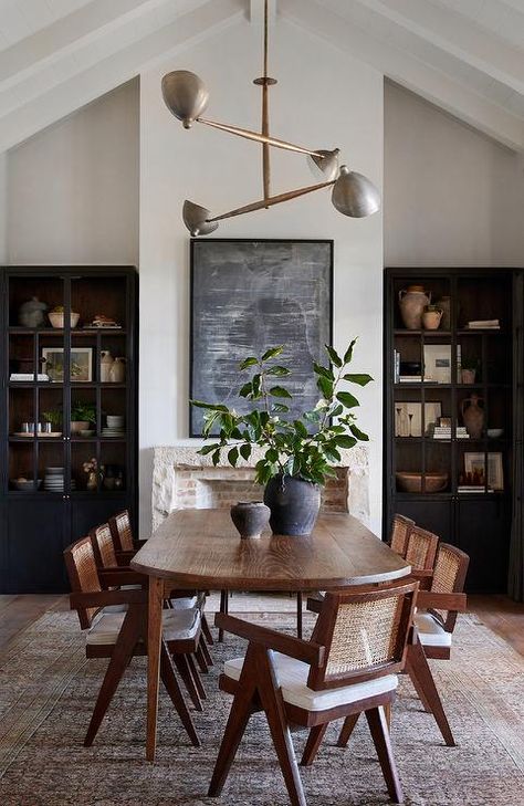 An oval oak dining table sits on a black and brown vintage rug surround by rope and wood dining chairs and is positioned in front of a rustic stone fireplace fixed beneath an abstract black art piece. Dark Wood Dining Table, Oval Dining Room Table, Dark Dining Room, Cottage Dining Rooms, Brown Dining Table, Wood Dining Room Table, Wood Dining Room, Vintage Dining Room, Dining Table Black