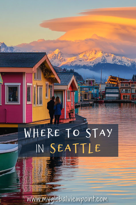 A couple walks along the waterfront by colorful houseboats in Seattle, with a stunning backdrop of snow-capped mountains and a dramatic sunset sky, highlighting one of the most beautiful places to stay in Seattle. Where To Stay In Seattle, Seattle Vacation, The Emerald City, Olympic National Park, Emerald City, Planning A Trip, Travel Itinerary, City Life, City Guide