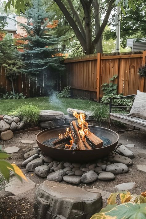 A cozy backyard with a fire pit surrounded by rocks, a wooden fence, and lush green trees and plants, perfect for relaxing outdoors. Outside Rock Fire Pit Ideas, Diy Fire Pit Sitting Area, Circle Fire Pit Area Diy, Pea Gravel Fire Pit Area Diy, Gravel Bonfire Pit, Fire Pit Circle Ideas, How To Level Ground For Fire Pit Area, Cool Backyard Features, Creekside Fire Pit