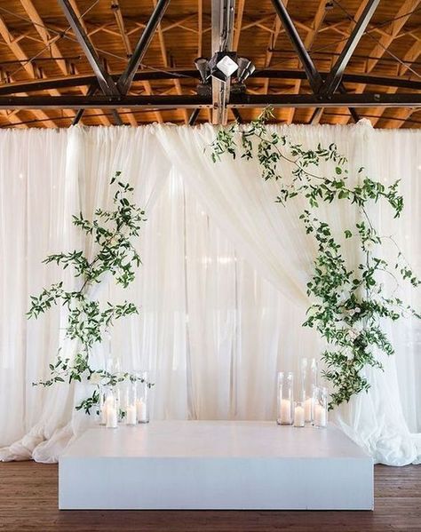 a minimalist wedding altar a white platform, candles, greenery hanging on curtains Wedding Ceremony Wall Backdrop, Hanging Greenery Wedding Arch, Modern Ceremony Backdrop, Wedding Ceremony Backdrops, Candles Reception, Modern Greenery, Draping Wedding, Wedding Ceremony Ideas, Simple Elegant Wedding