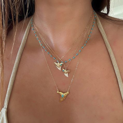 Turquoise Shark Tooth Necklaces. We know you will want to swim in the ocean with your shark tooth necklace so we used waterproof vermeil gold for this piece, and we always use authentic stones, so our turquoise is 100% real Arizona turquoise.The shark teeth we use are found on the shores of Florida and are all a bit different in size and shape. You will receive one shark tooth necklace. Gold with turquoise and white tip. Some photos show other pieces as layering options and styling inspiration. Gold And Turquoise Jewelry, Shark Tooth Necklace Gold, Swim In The Ocean, Surf Jewelry, Ocean Inspired Jewelry, Shark Necklace, Beachy Jewelry, Pretty Jewelry Necklaces, Shark Tooth Necklace