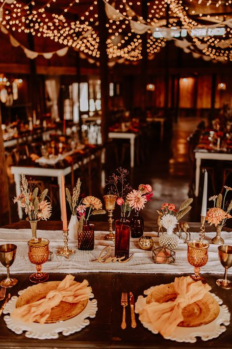 Sweetheart table at Boho styled wedding reception with amber, brass, and milkglass vessels. Amber Glass Wedding Tables, Farm Table Fall Decor, Fall Farm Table Wedding Decor, Vintage Table Wedding Decorations, Wedding Tables With Brass Candlesticks, Brown Glass Wedding Centerpieces, Boho Vintage Wedding Table, Brown Table Wedding Decor, Amber Glass Wedding Table