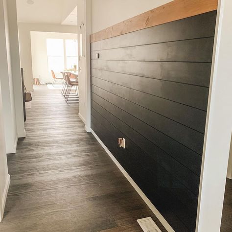 This entryway hallway with wood flooring boasts a white wall with horizontal black shiplap half wall. The half wall is topped by a stained wood plank used as a decorative trim. Black Shiplap Dining Room Wall, Accent Wall Ideas Half Wall, Half Wall Hallway, Dark Gray Shiplap Wall, Brown Shiplap Wall, Black Trim White Walls, Shiplap Half Wall, Shiplap Hallway, Black Shiplap Wall