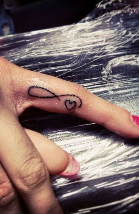 50 Powerful Infinity Tattoo Designs & Meaning - The Trend Spotter Ears Tattoo, Inner Finger Tattoo, Heart With Infinity Tattoo, Infinity Tattoo With Feather, Heart Tattoo On Finger, Love Heart Tattoo, Tattoos For Women Small Meaningful, Kids Ring, Tattoo Finger