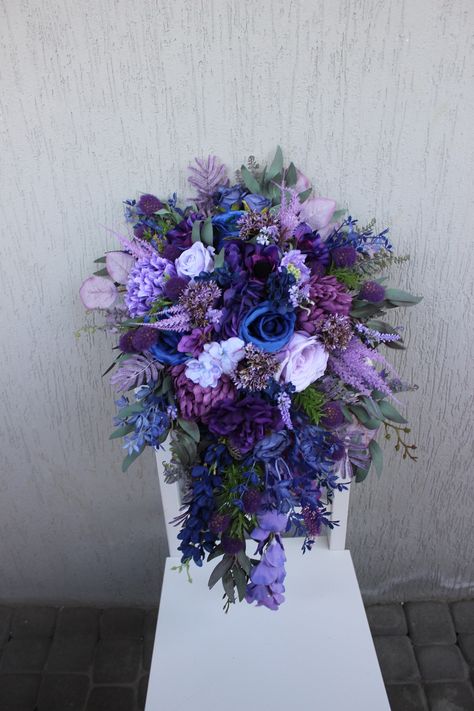 Immerse yourself in the enchanting beauty of our exquisite bouquet featuring jewel-toned hues. This cascading bridal bouquet, adorned in a blend of navy, purple silk flowers, roses, and eucalyptus, radiates elegance and sophistication, reflecting the unique beauty of your special day. From the bold tones of teal to the depths of purple, this artificial bouquet creates a refined arrangement that not only adds charm to your wedding ensemble but also serves as an unforgettable symbol of your love and unity. ○ Color: jewel tone, blue, navy, purple, lavender, green ○ Personalization: I can make changes to your wishes ○ Processing time: 1 - 2 weeks ○ Shipping time: 14 - 25 business days NOTE ○ I ship with REGISTERED mail and you will get a tracking number. ○ All items will be carefully packed in Navy Purple And Green Wedding, Purple Blue Centerpiece, Blue Purple Bouquet Wedding, Dark Blue Purple Wedding, Plum Purple And Navy Blue Wedding, Dark Blue And Dark Purple Wedding, Bridal Bouquet Fall Blue, Purple And Blue Floral Arrangements, Royal Purple And Navy Blue Wedding