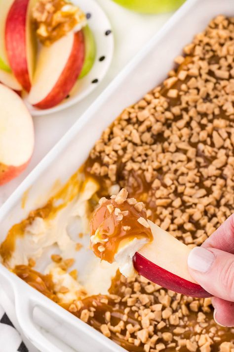 dipping a slice of apple into caramel apple dip. Apple Slices Dipped In Caramel, Apple Snicker Dip, Apple Dip Heath Bits, Apple Slices Dip, Apples Caramel Slices, Carmel Apple Heath Bar Dip, Apple Dip Caramel, Apple Dips Board, Caramel Apple Toffee Dip