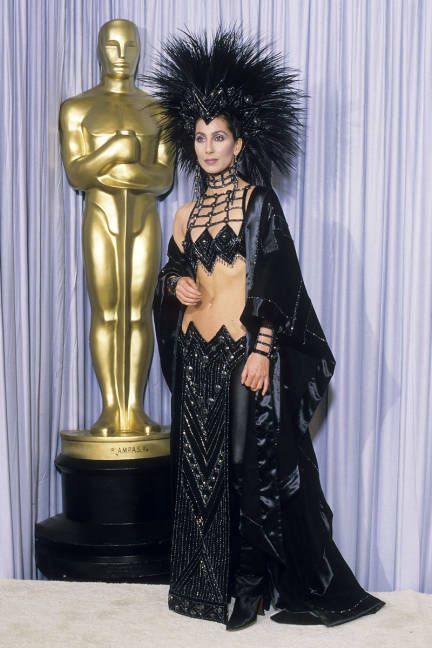 Cher at Oscars in 1986 (in midriff-bearing Bob Mackie getup featuring beaded loincloth, black cashmere cape, & mohowk-style headpiece made of hundreds of rooster feathers) Cher Black Outfit, Cher Bob Mackie, Oscars Fashion, Cher Fashion, Cher Looks, Cher Costume, Cher Outfits, Academy Awards Red Carpet, Cher Photos