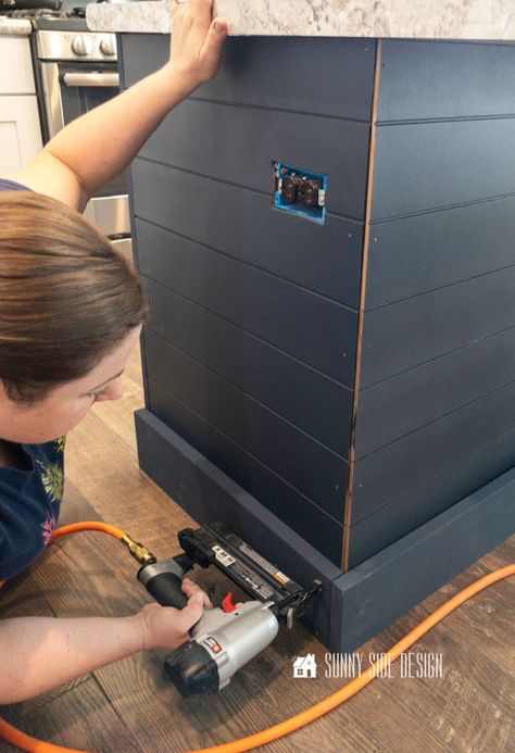 Woman holding a brad nailer secures the navy blue painted base molding to the bottom of the kitchen island. Kitchen Island With Shiplap, Island With Shiplap, Shiplap Bar, Kitchen Island Trim, Kitchen Island Base, Diy Kitchen Ideas, Shiplap Trim, Kitchen Island Makeover, Shiplap Kitchen