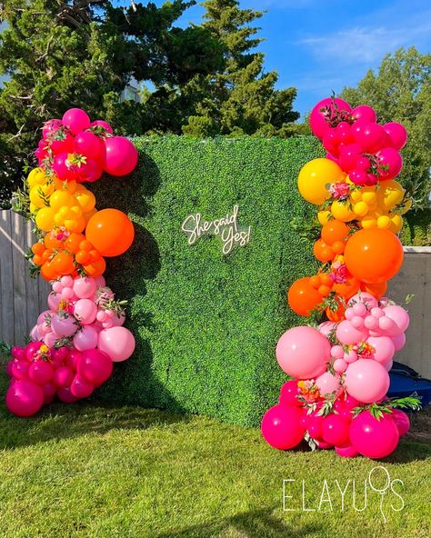 Bridal shower grass backdrop with colorful pink, orange and yellow balloons. Summer display Tiki Backdrop Ideas, Bright Colorful Centerpieces, Bright Pink Party Decorations, Balloon Garland Bright Colors, Pink Orange Yellow Balloons, Hawaiian Theme Balloon Garland, Pink Orange Yellow Balloon Garland, Hot Pink And Orange Balloons, Pink Yellow Orange Balloon Arch